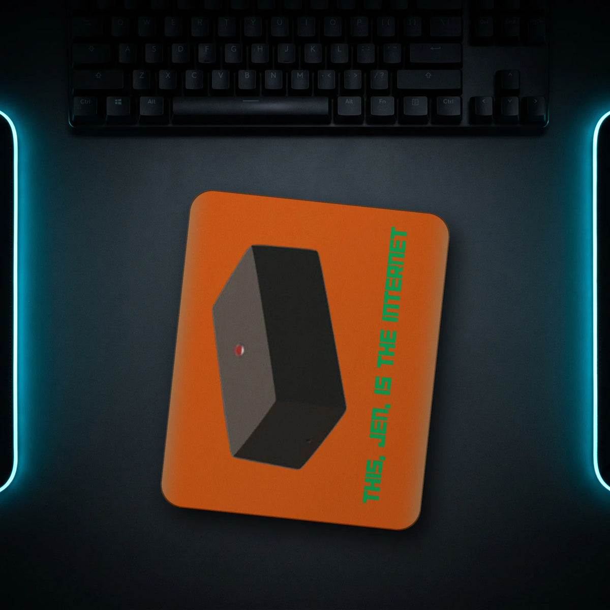 IT Meme mousepad with the "This, Jen, is the Internet" black box print, top-down on a dark desk next to a keyboard with cyan light strips